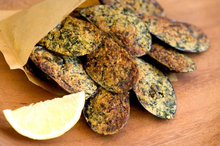 Kraft kâğıda sarılı, yeşil otlu çıtır krakerleri içeren tabak. Ahşap yüzeyde krakerlerin yanında taze limon dilimi duruyor. Sıcak, davetkar bir sunum. — KiKi, Sıraselviler 42, Cihangir, İstanbul