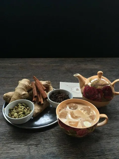 Koyu ahşap masada seramik çay seti: çiçek desenli kahverengi demlik, aynı desendeki fincan içinde çay, ginger ve tarçın çubukları, cardamom ve siyah çay yaprakları. — KiKi, Sıraselviler 42, Cihangir, İstanbul