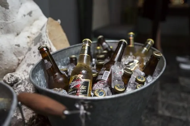 Metal bir teknede buz içinde bekleyen çeşitli bira şişeleri. Sağ tarafta Miller markası görülüyor. Arka planda bulanık iç mekân ve duvarlar. Gece mekanı ortamı, soğuk içecek servisi. — KiKi, Sıraselviler 42, Cihangir, İstanbul