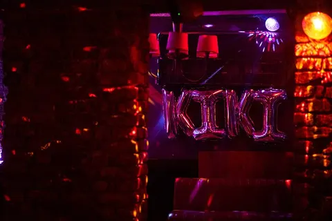 Koyu bir bar içinde pembe ve kırmızı neon ışıklar hakimdir. Siyah metal yapıda asılı kırmızı lambalar ve neon tüplerle yazılı mekân adı görülüyor. Turuncu ve mor renkli ışık demeti tavandan yayılmaktadır. Koyu atmosferde sadece ışıklar belirgin şekilde parlıyor. — KiKi, Sıraselviler 42, Cihangir, İstanbul