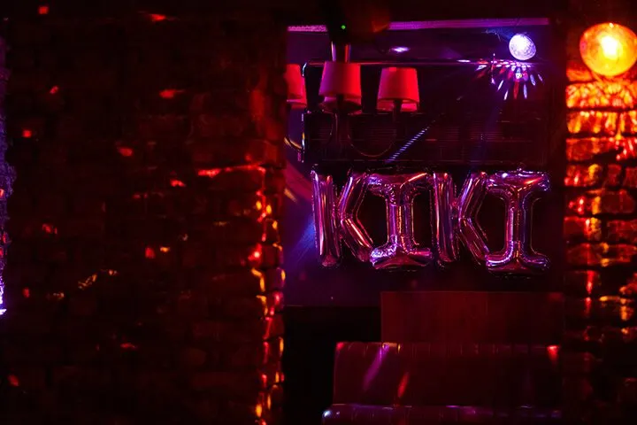 Koyu bir bar içinde pembe ve kırmızı neon ışıklar hakimdir. Siyah metal yapıda asılı kırmızı lambalar ve neon tüplerle yazılı mekân adı görülüyor. Turuncu ve mor renkli ışık demeti tavandan yayılmaktadır. Koyu atmosferde sadece ışıklar belirgin şekilde parlıyor. — KiKi, Sıraselviler 42, Cihangir, İstanbul