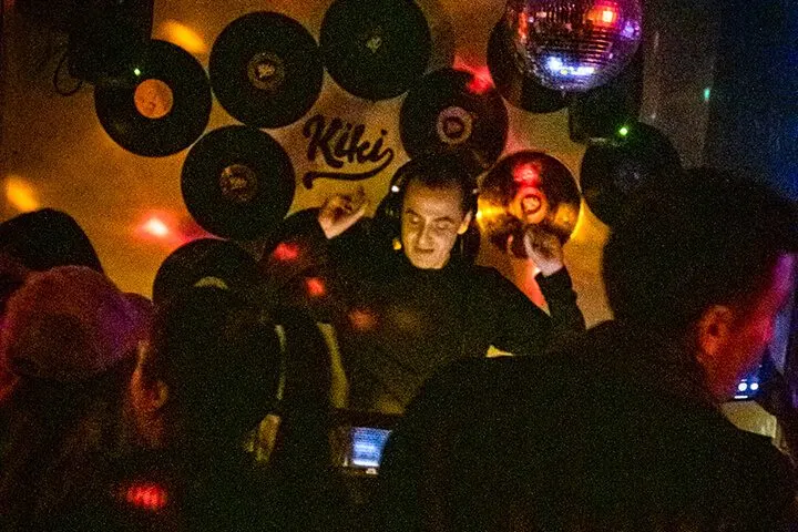 Siyah vinilplaklar duvar dekorasyonu olarak asılı. Renkli ışıklar kırmızı, mavi, sarı tonlarında parıldıyor. Kalabalık insanlar karanlık ortamda dans ediyor. Disco topu üst kısımda ışık yayıyor. Bazı kişiler telefon çekiyor. — KiKi, Sıraselviler 42, Cihangir, İstanbul