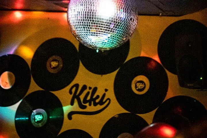 Sarı duvar üzerine asılı siyah vinil plaklar arasında parlayan bir disko topu. Kırmızı, turuncu ve yeşil renkli sahne ışıkları gece mekanının atmosferini yaratıyor. Plakalar daire şeklinde düzenlenmiş, merkezdeki disko topundan yansıyan ışın kütleleri görülüyor. — KiKi, Sıraselviler 42, Cihangir, İstanbul