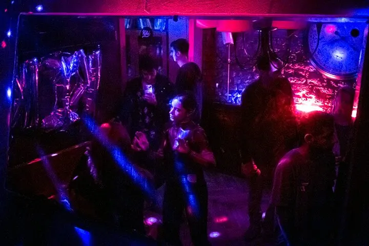 Mor ve mavi neon ışıklarla aydınlanan dar bir mekanın içinde, birbirine yakın duran ve dans eden insanlar. Arka planda parlak pembe ve mavi LED paneller, tavanda ve çevrede renkli ışık kaynakları görülüyor. İnsanlar silüet halinde. — KiKi, Sıraselviler 42, Cihangir, İstanbul