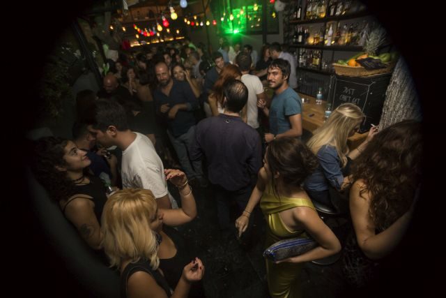 Dar, loş bir mekanın içinde yoğun kalabalık. Yeşil neon ışık ve sıcak sarı aydınlatma. İnsanlar birbirine yakın dans ediyor, müzik dinliyor. Arka planda bar tezgahı ve şişeler görünüyor. — KiKi, Sıraselviler 42, Cihangir, İstanbul
