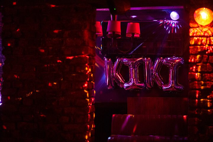 Koyu bir bar içinde pembe ve kırmızı neon ışıklar hakimdir. Siyah metal yapıda asılı kırmızı lambalar ve neon tüplerle yazılı mekân adı görülüyor. Turuncu ve mor renkli ışık demeti tavandan yayılmaktadır. Koyu atmosferde sadece ışıklar belirgin şekilde parlıyor. — KiKi, Sıraselviler 42, Cihangir, İstanbul